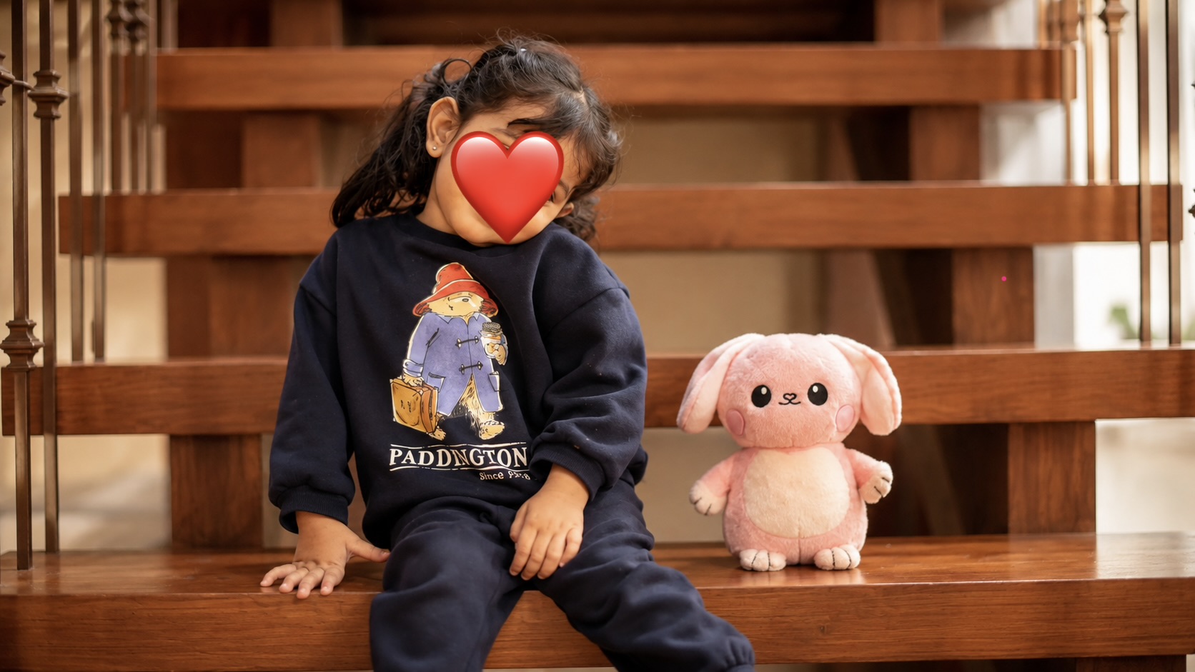 A young child sitting on polished wooden stair steps at home, a pink Glow Buddy bunny resting beside them.